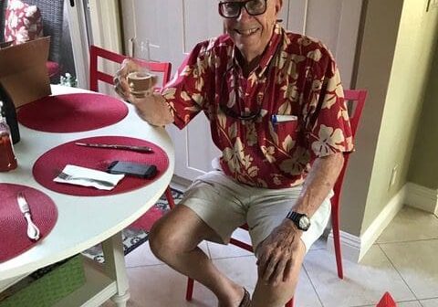 Man in a red shirt smiles while drinking.