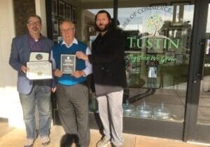 Three men holding awards in front of a building.